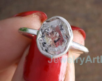 May include: A silver ring with a clear, faceted gemstone set in a bezel setting. The gemstone has a cloudy, milky appearance with inclusions.