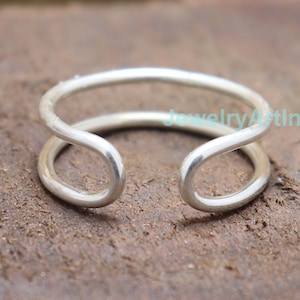 May include: A silver ring with a double band design. The ring is open on one side, making it adjustable.