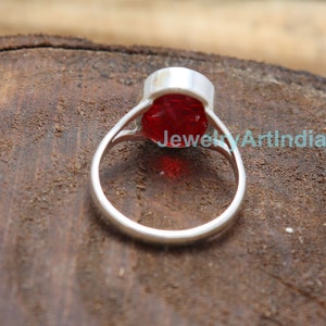 Op de afbeelding: Een zilveren ring met een grote, rode, gefacetteerde edelsteen. De ring ligt op een houten oppervlak.