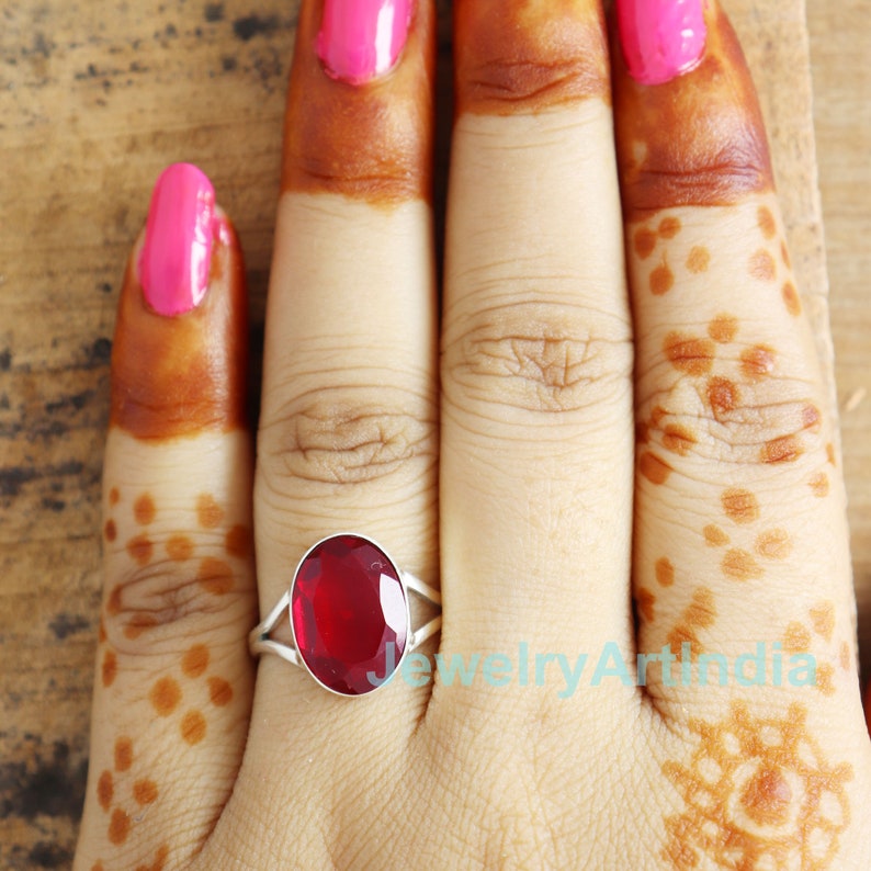 Op de afbeelding: Een zilveren ring met een grote, ovale, rode edelsteen. De ring zit aan een vinger met henna.