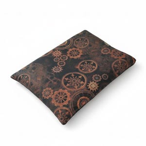 Peut inclure: Un coussin rectangulaire marron foncé avec un motif répété d'engrenages et de roues dentées de couleur bronze. Le coussin a une esthétique steampunk, avec un aspect texturé et vieilli. Les engrenages varient en taille.