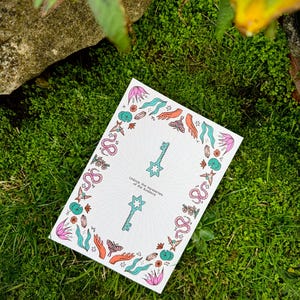 May include: A white card with a colorful border of leaves, butterflies, and snakes, resting on green grass. The card features two keys and the text "Unlock the mysteries of the cosmos."