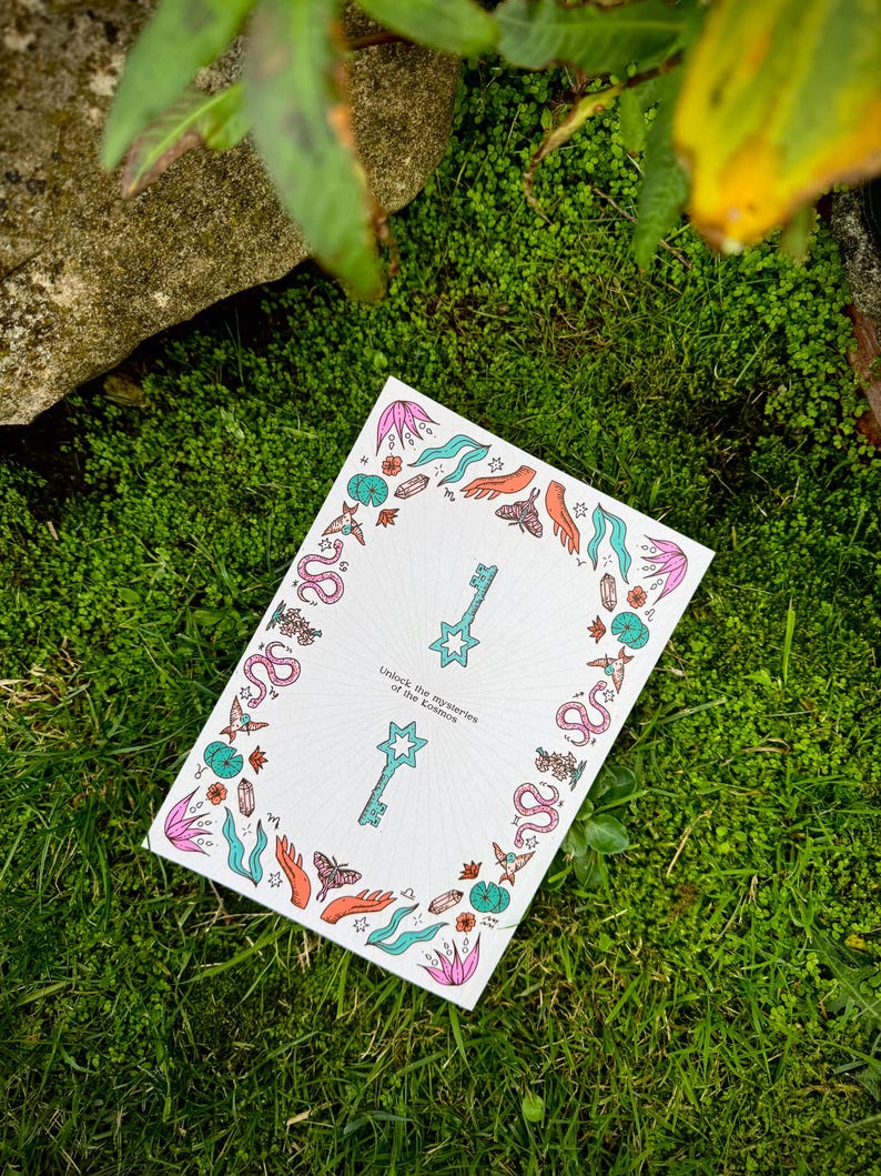 May include: A white card with a colorful border of leaves, butterflies, and snakes, resting on green grass. The card features two keys and the text "Unlock the mysteries of the cosmos."