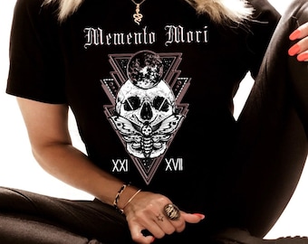 May include: A black short-sleeve t-shirt featuring a white graphic print of a skull, a moth, and a moon inside a geometric triangle frame. The text "Memento Mori" is printed above the graphic, with the Roman numerals "XXI" and "XVII" below.