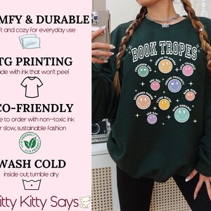 May include: Forest green sweatshirt with the text "BOOK TROPES" and various smiley face graphics. The sweatshirt also features text such as "Enemies to Lovers" and "Forced Proximity". The sweatshirt is made with DTG printing and eco-friendly ink.