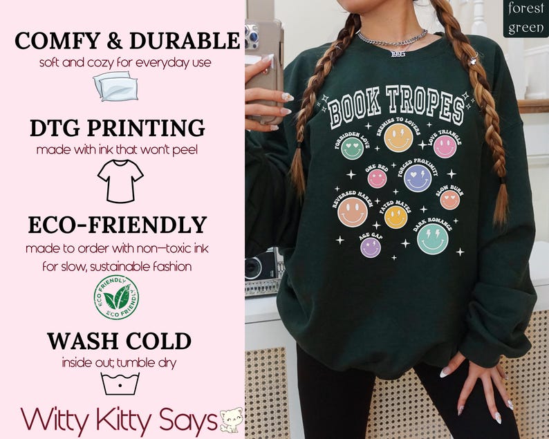 May include: Forest green sweatshirt with the text "BOOK TROPES" and various smiley face graphics. The sweatshirt also features text such as "Enemies to Lovers" and "Forced Proximity". The sweatshirt is made with DTG printing and eco-friendly ink.