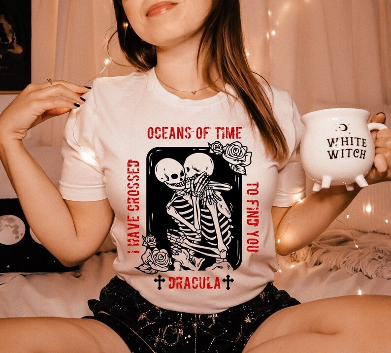 May include: White t-shirt with a black and white graphic of two skeletons embracing. The graphic includes the text "I have crossed oceans of time to find you" and "Dracula".