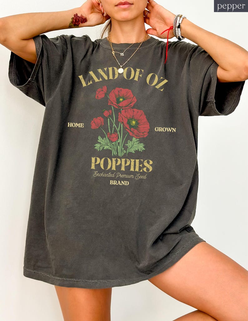 May include: Dark gray oversized t-shirt with a graphic featuring red poppies and the text "LAND OF OZ POPPIES." The design includes the words "HOME GROWN" and "Enchanted Premium Seed BRAND" in a vintage style.
