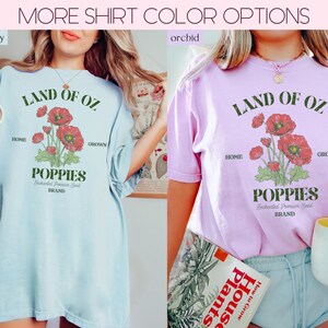 May include: Two t-shirts, one light blue and one orchid, with the text "LAND OF OZ" and a graphic of red poppies. The shirts also feature the words "HOME" and "GROWN" and the word "POPPIES". The text "Enchanted Premium Seed BRAND" is also visible.
