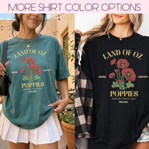 May include: Two t-shirts, one blue-green and one black, each with a graphic featuring the text "LAND OF OZ" above a floral illustration of red poppies. Below the flowers, the word "POPPIES" is displayed. The shirts are short-sleeved.