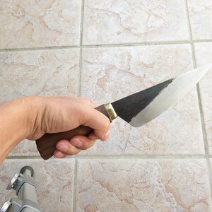 May include: A hand holding a knife with a wooden handle and a black and silver blade.