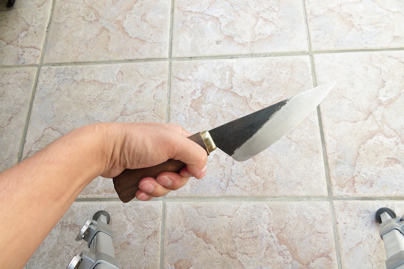 May include: A hand holding a knife with a wooden handle and a black and silver blade.