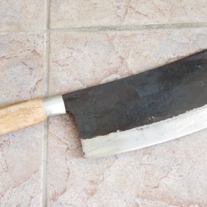 May include: A large, black cleaver with a wooden handle. The blade is sharp and has a slight curve. The handle is made of wood and has a metal cap on the end.