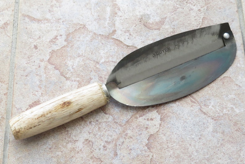 May include: A wooden handled stainless steel apple peeler with the word "SPUYEN" printed on the blade.