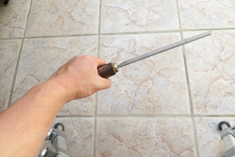 Peut inclure: Une main tient une lime en m&eacute;tal avec un manche en bois. La lime mesure environ 30 cm de long et a une lame plate et rectangulaire.