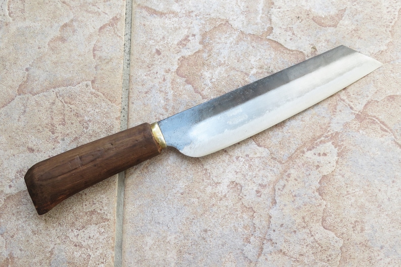 Peut inclure: Un couteau long et fin, en argent, avec un manche en bois. Le couteau a une lame l&eacute;g&egrave;rement incurv&eacute;e et un accent en laiton &agrave; la base de la lame.