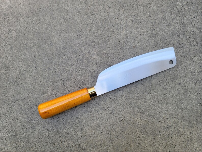 May include: A stainless steel cleaver knife with a light brown wooden handle and a gold-coloured bolster. The blade is wide and straight, with a hole near the tip. The knife is designed for chopping and slicing.
