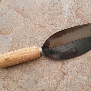 May include: A wooden handled metal vegetable peeler with a curved blade. The peeler is used for peeling vegetables and fruits.