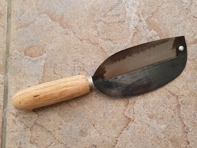 May include: A wooden handled metal vegetable peeler with a curved blade. The peeler is used for peeling vegetables and fruits.