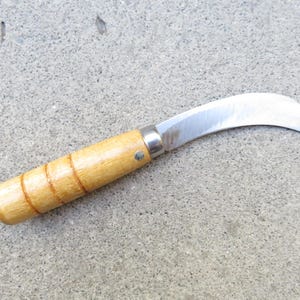May include: A curved blade knife with a wooden handle. The blade is made of shiny metal and has a curved shape. The handle is light brown with three carved rings. The knife is designed for gardening or other cutting tasks.