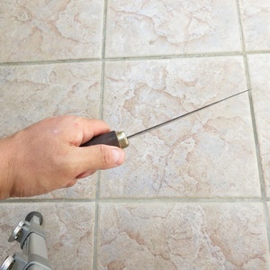 May include: A long, thin, silver knife with a dark brown wooden handle. The knife is held in a hand with the blade pointing towards the right.