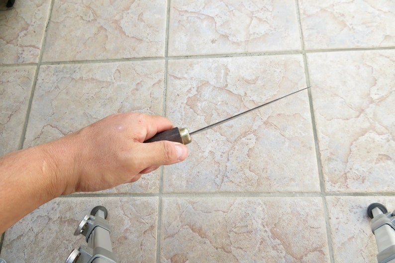May include: A long, thin, silver knife with a dark brown wooden handle. The knife is held in a hand with the blade pointing towards the right.