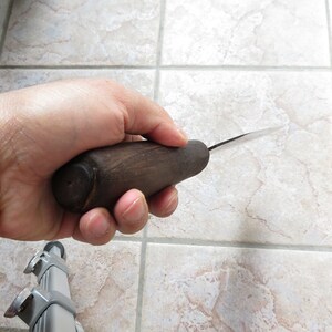 May include: A close-up of a hand holding a wooden-handled carving knife with a thin, sharp blade.