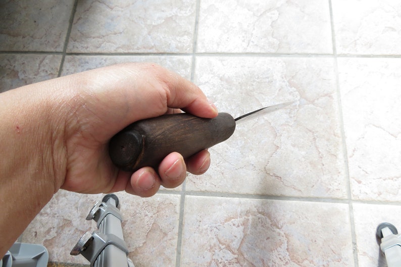May include: A close-up of a hand holding a wooden-handled carving knife with a thin, sharp blade.