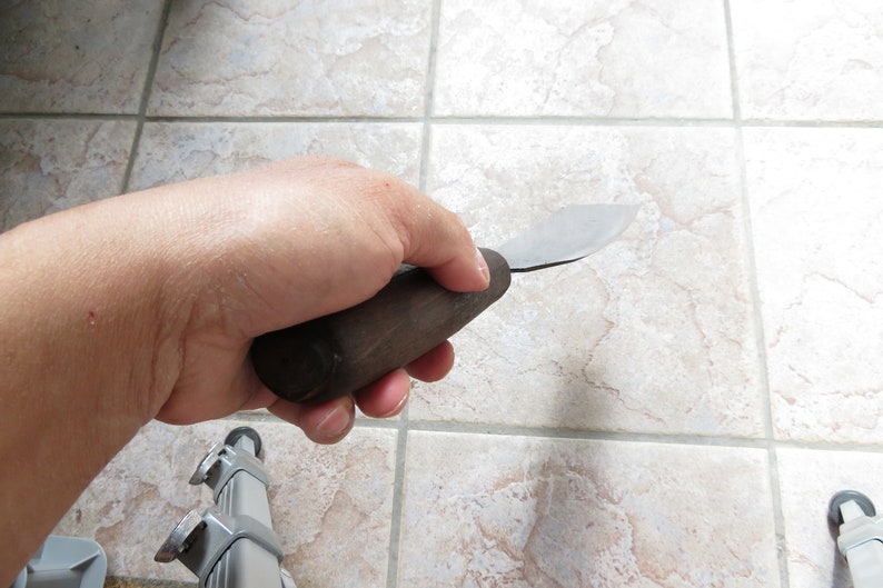 May include: A hand holding a small, wooden-handled, metal scraper tool.