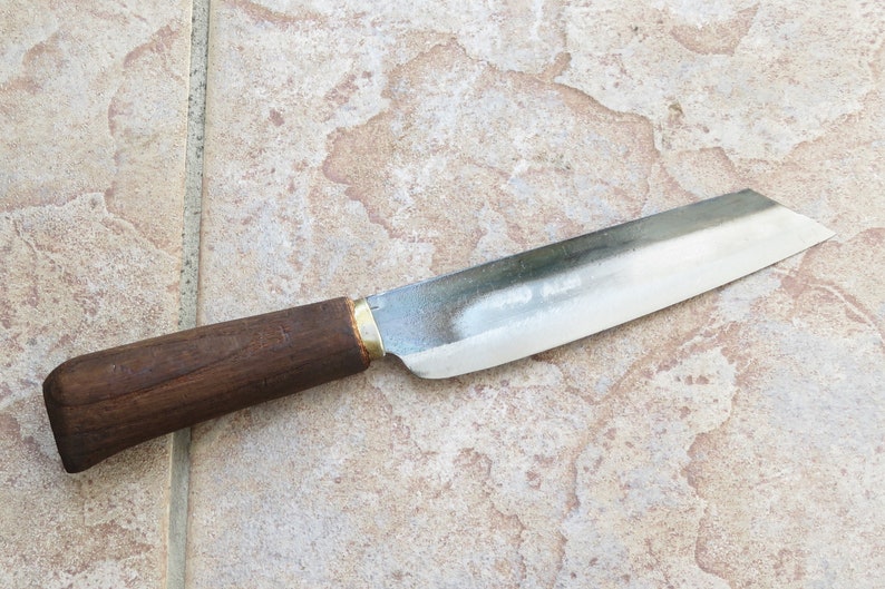 May include: A knife with a brown handle and a silver blade. The knife is lying on a light brown tiled surface.