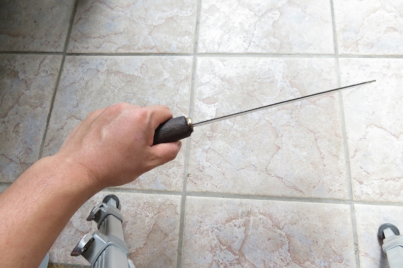 May include: A person holding a long, thin, silver knife with a brown wooden handle.
