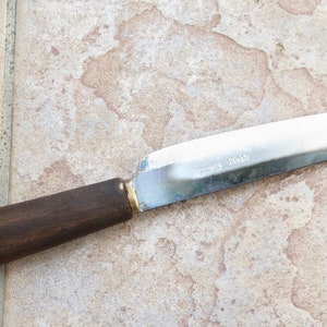May include: A knife with a brown wooden handle and a silver blade. The blade is etched with the words "Made in Japan".
