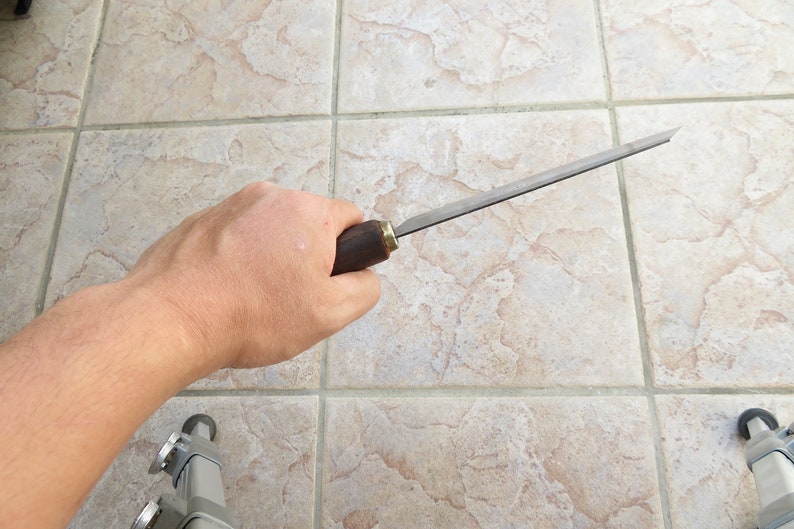 May include: A person holding a long, thin, metal file with a wooden handle. The file has a brass ferrule at the end of the handle.
