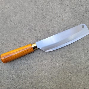 May include: A stainless steel cleaver knife with a polished blade and a wooden handle. The handle is light brown with a gold-coloured metal bolster. The knife has a hole near the tip of the blade.