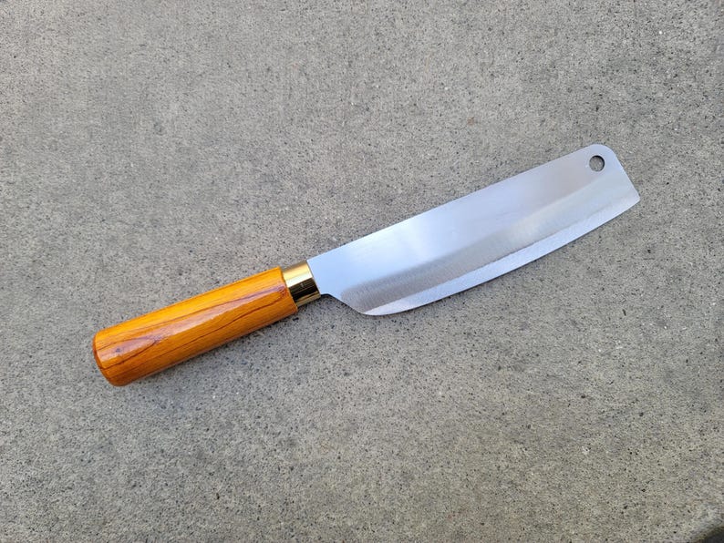 May include: A stainless steel cleaver knife with a polished blade and a wooden handle. The handle is light brown with a gold-coloured metal bolster. The knife has a hole near the tip of the blade.