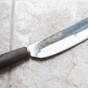 May include: A large, heavy-duty knife with a wooden handle and a slightly curved blade. The blade is dull and has a patina of rust.