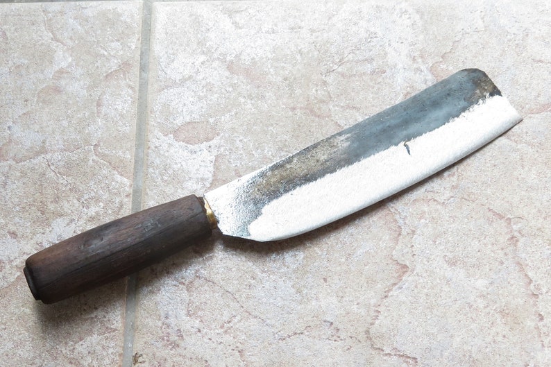 May include: A large, heavy-duty knife with a wooden handle and a slightly curved blade. The blade is dull and has a patina of rust.