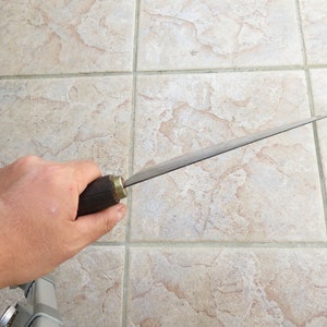 Puede incluir: Una persona sosteniendo un cuchillo largo, delgado y plateado con un mango de madera oscura. El cuchillo tiene una punta afilada y un filo recto.