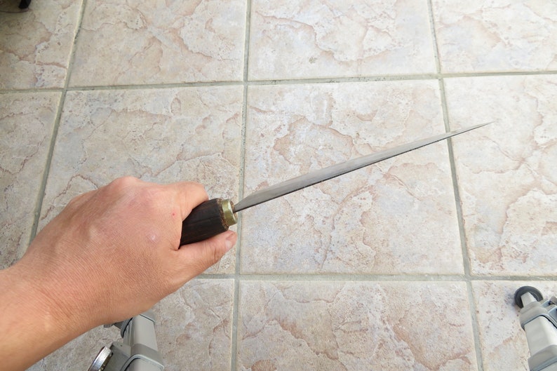 Puede incluir: Una persona sosteniendo un cuchillo largo, delgado y plateado con un mango de madera oscura. El cuchillo tiene una punta afilada y un filo recto.