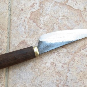 May include: A small, sharp knife with a wooden handle and a metal blade. The blade is slightly curved and has a dull finish. The handle is dark brown and has a brass ferrule.