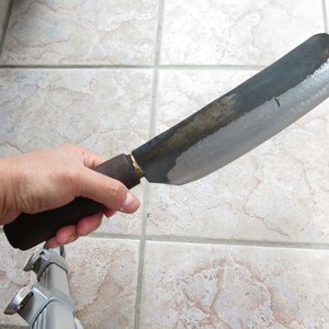 May include: A large, curved, black metal knife with a wooden handle. The blade is dull and has a slight patina.