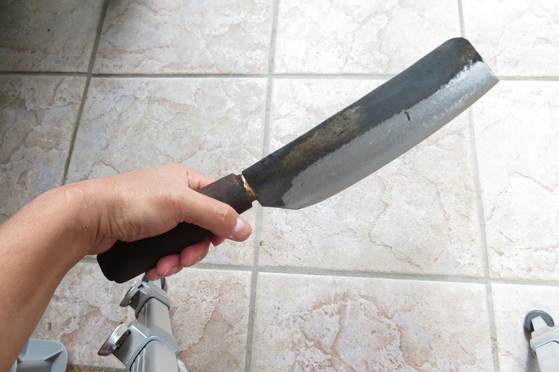 May include: A large, curved, black metal knife with a wooden handle. The blade is dull and has a slight patina.