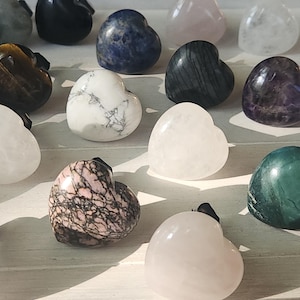 May include: A collection of heart-shaped stones in various colors and patterns. The stones include white, pink, blue, green, and black, with unique veining and textures. Each stone has a small black attachment.