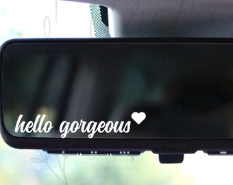 May include: A rearview mirror with a white vinyl sticker that says "hello gorgeous" with a small heart symbol.