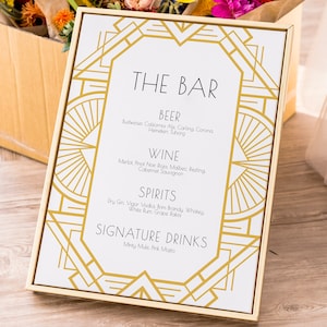 May include: A gold framed sign with an art deco design. The sign reads "The Bar" and lists various beer, wine, and spirit options. The sign also includes a section for signature drinks, which are "Minty Mule" and "Pink Mojito".