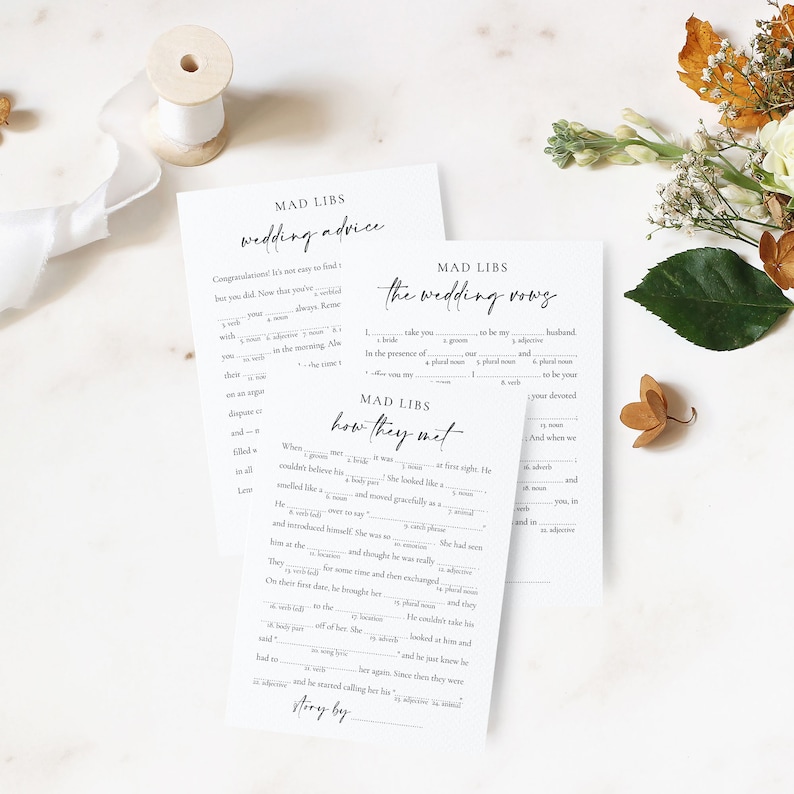 3 printable mad libs games laying together on a white marble background with dried flowers and a lace ribbon