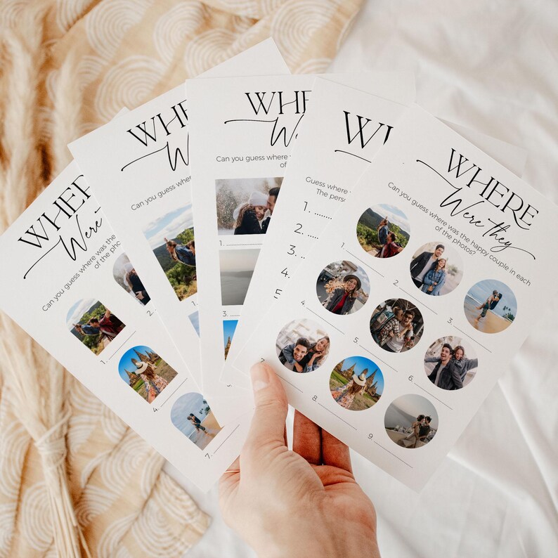 A hand holding 5 "where were they" wedding game cards with modern, minimalist design and beautiful, written calligraphy font