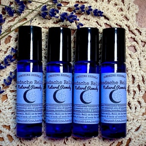 Puede incluir: Cuatro botellas de vidrio azul con rodillo y una etiqueta blanca que dice "Sunshine Herbals Headache Relief Natural Remedy". Las botellas est&aacute;n dispuestas en fila sobre una superficie de crochet blanco.