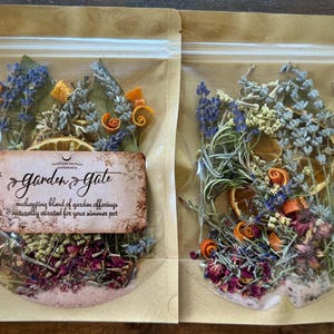 May include: Two clear plastic bags filled with dried flowers and herbs. The bags contain lavender, orange peel curls, and rose petals. One bag has a label that reads "Garden Gate" and "enchanting blend of garden offerings naturally curated for your simmer pot."
