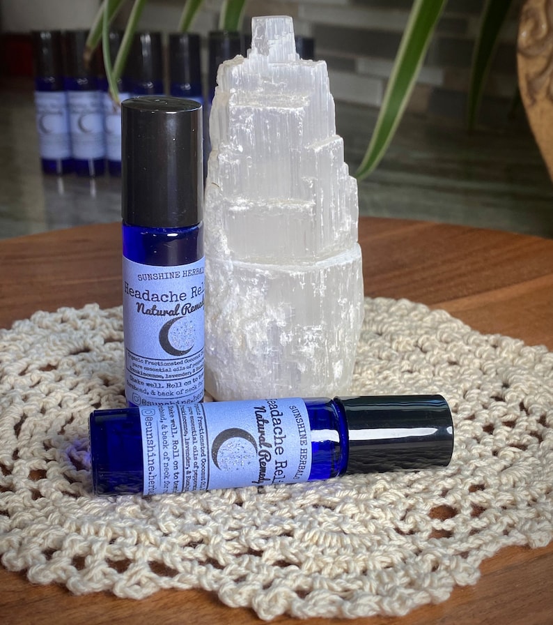 Puede incluir: Dos botellas de vidrio azul con tapones negros y etiquetas blancas que dicen "Headache Relief Natural Remedy" con un gr&aacute;fico de luna creciente y estrellas. Las botellas est&aacute;n sobre un encaje blanco de ganchillo.